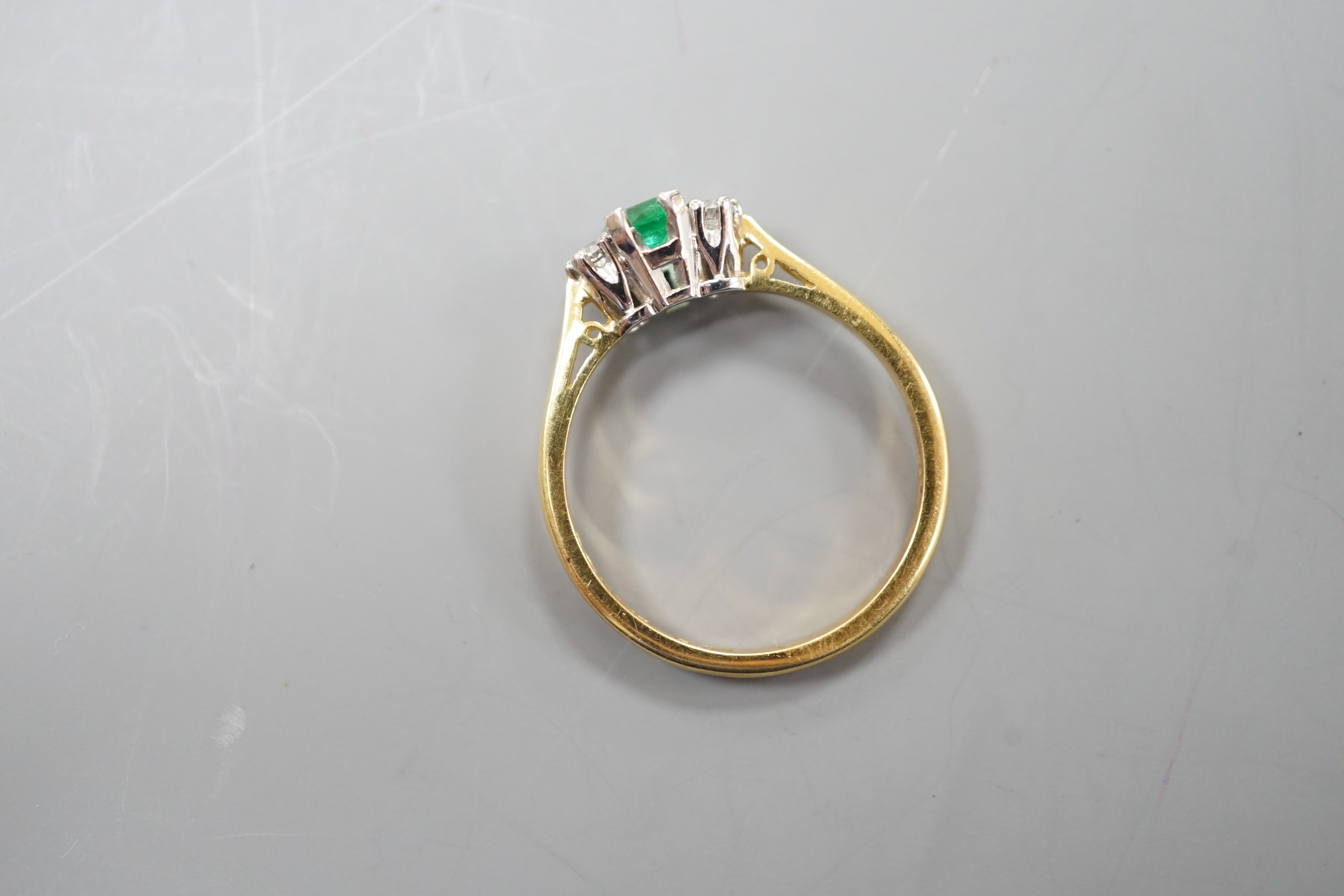 A modern 18ct gold, emerald and diamond set three stone ring, size N, gross weight 2.6 grams.